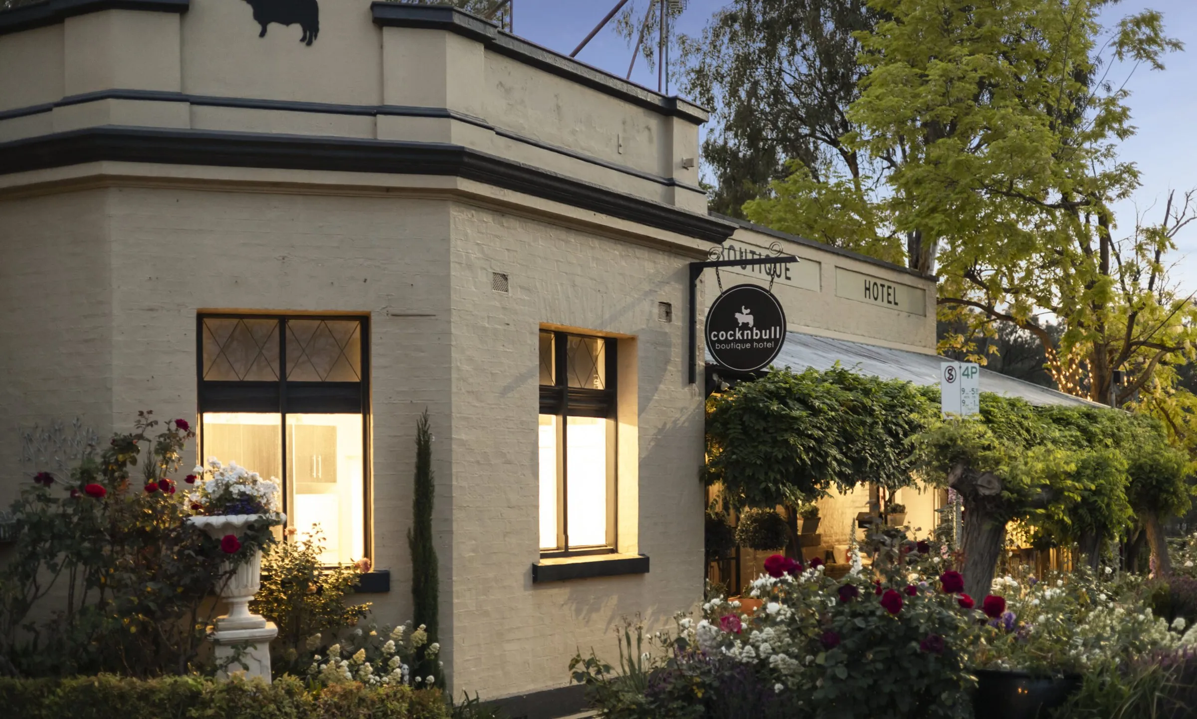 The hotel's corner facade at dusk, lamplit windows above a rose garden