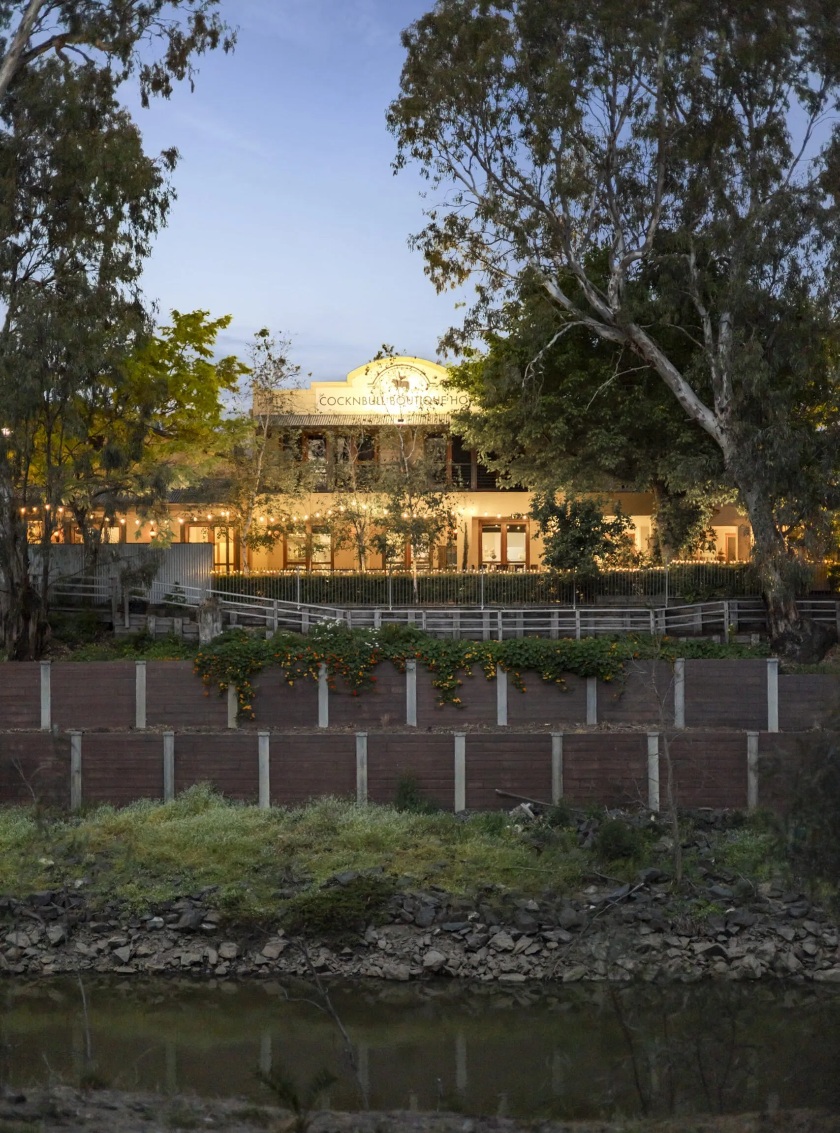 The hotel seen from across the Campaspe River at dusk, lights on along the verandah